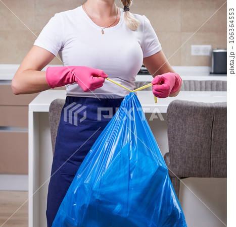 Housewife wearing protective rubber gloves holding garbage bag standing in a kitchen. Cleaning service concept 106364553