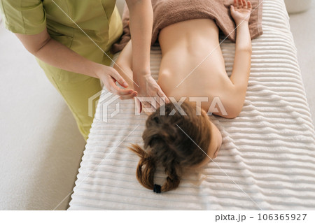 High-angle view of unrecognizable female pediatric masseuse doing therapeutic massage to relax shoulder joint and shoulder blade of little girl. Kid client get service massage in spa salon. High-angle view of unrecognizable female pediatric masseuse doing therapeutic massage to relax shoulder joint and shoulder blade of little girl. Kid client get service massage in spa salon. 106365927