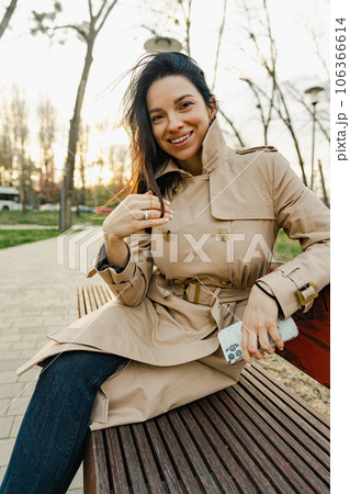 Beautiful young woman in coat relaxing on a bench in park Beautiful young woman in coat relaxing on a bench in park 106366614