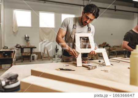 Young man carpenter wearing uniform working in joinery making wooden furniture 106366647