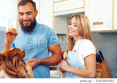 Happy couple cooking food at kitchen with their dog 106366892