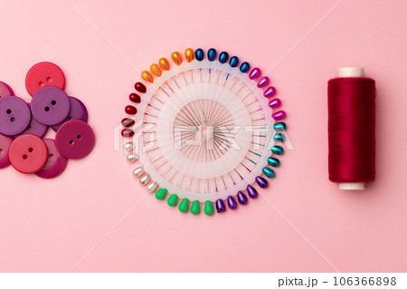 Sewing accessories including thread spools and pins on pink background 106366898