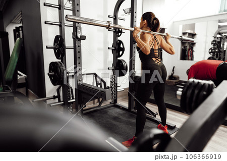 Fit woman doing squats with barbell in a gym 106366919