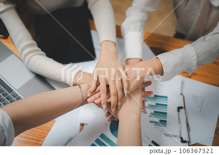Positive diverse business team putting their hands on top of each other, showing unity and teamwork Positive diverse business team putting their hands on top of each other, showing unity and teamwork 106367321