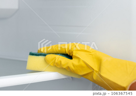 Hand of a woman in yellow glove cleaning the fridge shelf Hand of a woman in yellow glove cleaning the fridge shelf 106367545