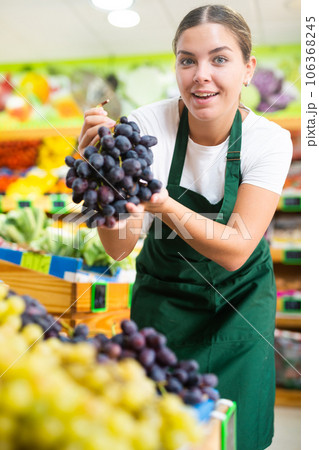 Happy young female seller demonstrating grape in grocery shop Happy young female seller demonstrating grape in grocery shop 106368245