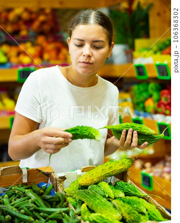 Dissatisfied young female customer buying bitter gourd in shop Dissatisfied young female customer buying bitter gourd in shop 106368302