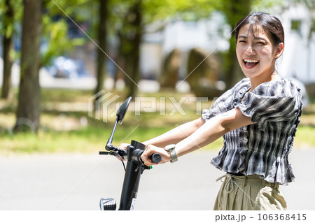 輝く陽射しと緑の木々の中を電動キックボードで爽やかに走る若くてかわいい女性|電動キックボードイメージ 輝く陽射しと緑の木々の中を電動キックボードで爽やかに走る若くてかわいい女性|電動キックボードイメージ 106368415