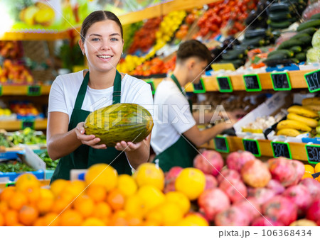 Friendly female vendor laying out ripe melon on counter Friendly female vendor laying out ripe melon on counter 106368434