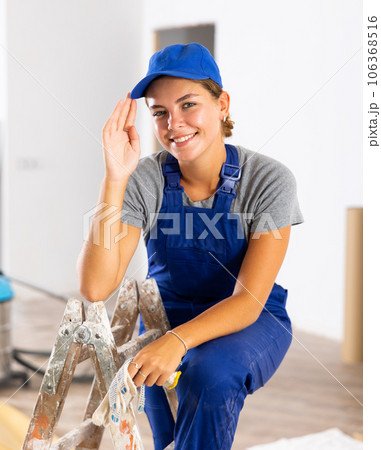 Portrait of positive builder woman in blue overalls next to stepladder Portrait of positive builder woman in blue overalls next to stepladder 106368516