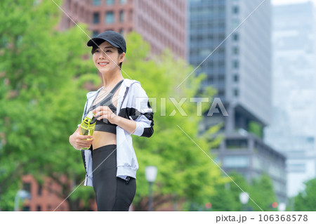 都会でジョギングの途中で休憩して水を飲む若い女性 106368578