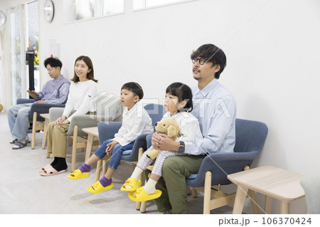 歯医者、クリニックの待合室でテレビを見ながら待つ親子と男性患者 106370424