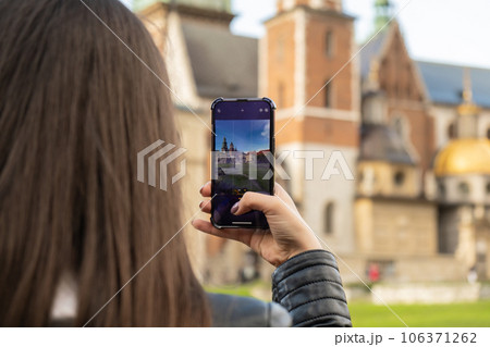 Female traveler in historical places looks around courtyard of landmark and shoots short video on phone. Unrecognizable woman Tourist photographs historic place on sunny day. Tourism and blogging 106371262