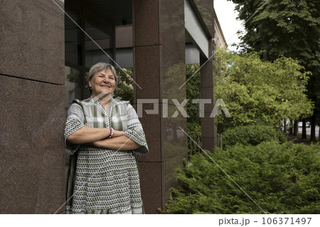 Real Cheerful Smiling Senior Woman In Yard Of Modern Building. Green Bushes Around. Copy Space For Text. Pleased Elderly 70s Carefree. Beautiful Granny Looking Away Horizontal Plane, Copy Space 106371497