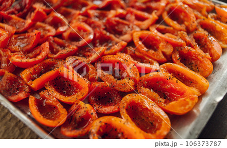 Sun-dried tomatoes on a baking tray. Fresh tomatoes sprinkled with aromatic seasonings. High quality photo 106373787