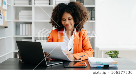 Young African woman typing on tablet and laptop while sitting at the working black table office.. 106377536