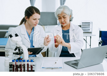 Two scientist or medical technician working, having a medical discuss meeting with an Asian senior female scientist supervisor in the laboratory with online reading, test samples and innovation for 106378606