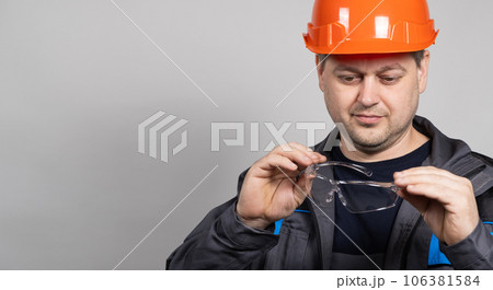 A construction worker in a helmet and overalls put on goggles protective glasses on a white background. A construction worker in a helmet and overalls put on goggles protective glasses on a white background. 106381584