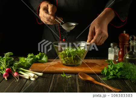 The chef peppers chopped lettuce leaves in a bowl. Working environment in a restaurant kitchen. Delicious salad with fresh vegetables 106383383