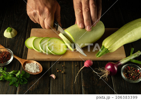 The chef cuts the zucchini into small pieces with a knife before preparing a delicious dinner with vegetables. National food 106383399