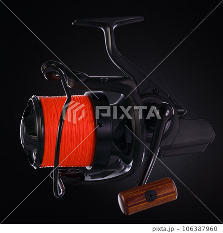 Black fishing reel with orange fishing line, on a black background. Close-up 106387960