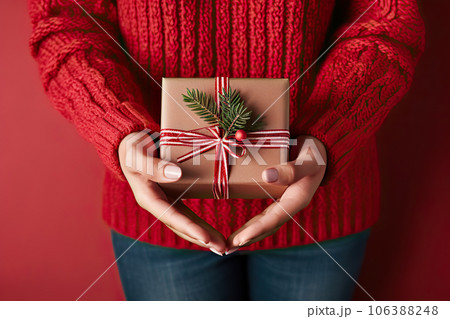 Festive Gift Giving Female's Hands Holding Christmas Gift Box with Evergreen Branch on Red Background. created with Generative AI Festive Gift Giving Female's Hands Holding Christmas Gift Box with Evergreen Branch on Red Background. created with Generative AI 106388248