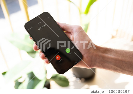 Fraud or fraudulent schemes. Close-up of a male hand holding a phone with an unexpected incoming call from an unknown 106389197