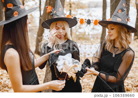 Three young girls witches in forest on Halloween. Girls wearing in black dresses and cone hat. Witch holding a magician stuff. 106389660