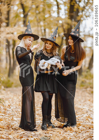 Three young girls witches in forest on Halloween. Girls wearing black dresses and cone hat. Witches holding a magician cauldron. Three young girls witches in forest on Halloween. Girls wearing black dresses and cone hat. Witches holding a magician cauldron. 106389665