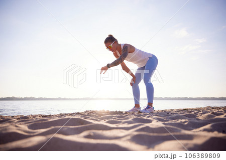 Full-lenght portrait of active woman runner in sport clothes checking athletic tracker on seashore. Woman resting after morning fitness routine. Full-lenght portrait of active woman runner in sport clothes checking athletic tracker on seashore. Woman resting after morning fitness routine. 106389809
