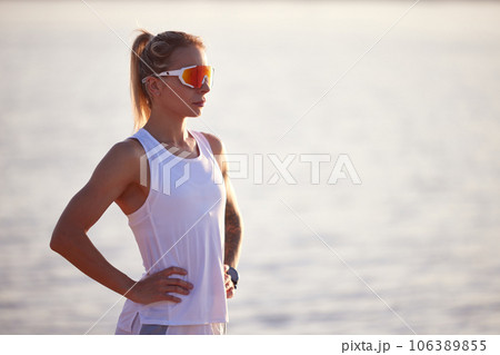 Portrait of active woman runner in sport clothes and sunglasses on seashore. Woman relaxing, resting after morning fitness routine. 106389855