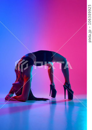 Full size portrait of young beautiful slim girl dancer on high heels dancing in bridge pose on the floor in blue-pink neon light. 106389925
