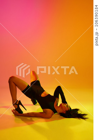 Side view portrait of young girl dancing heels dance in stylish clothes on floor in colorful mixed neon light. Expressive hobby. 106390184