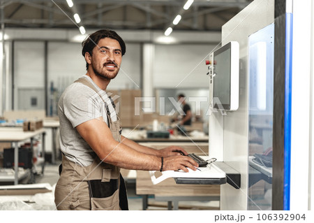 Young carpenter operating machine for wood processing at a furniture factory Young carpenter operating machine for wood processing at a furniture factory 106392904