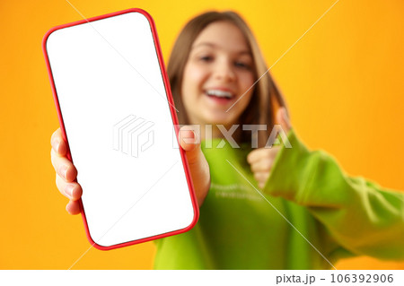 Teen girl showing smartphone screen with copy space over yellow background Teen girl showing smartphone screen with copy space over yellow background 106392906