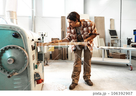 Young carpenter working on woodworking machines in the furniture factory Young carpenter working on woodworking machines in the furniture factory 106392907