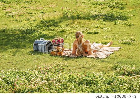 Girl relaxing with her dog on picnic on the green grass, summer day 106394748
