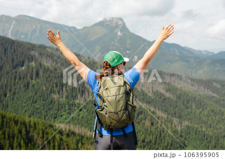 Woman hiker with backpack open arms at mountain peak. Travel and active lifestyle concept. 30s girl enjoying valley view from top of a mountain, outdoor activities 106395905