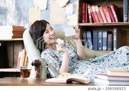 お菓子を食べながらスマホで映画を見る女性 106398925