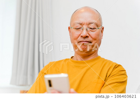 老眼鏡をかけスマートフォンの画面を遠ざけて操作する初老の男性 老眼鏡をかけスマートフォンの画面を遠ざけて操作する初老の男性 106403621