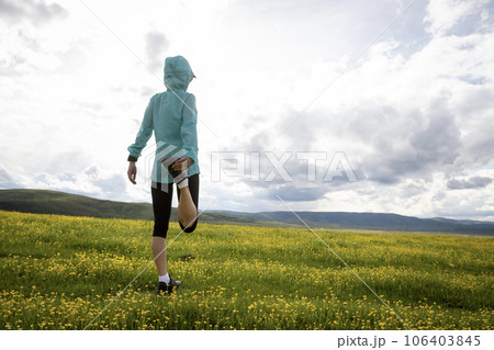 Woman trail runner stretching legs in flowers at high altitude grassland mountain Woman trail runner stretching legs in flowers at high altitude grassland mountain 106403845