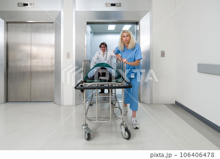 A nurse and doctor in propels a wheeled stretcher, carrying a patient out of the elevator to the emergency room of the hospital. 106406478