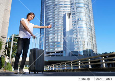 スーツケースを持って路上で車を呼び止める男性 106411864