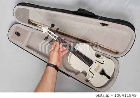 A man's hand takes a white violin out of its case 106411948