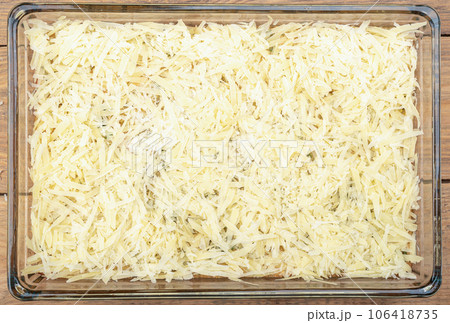 Unsweetened burek sprinkled with grated cheese in a glass baking dish on a wooden background. 106418735