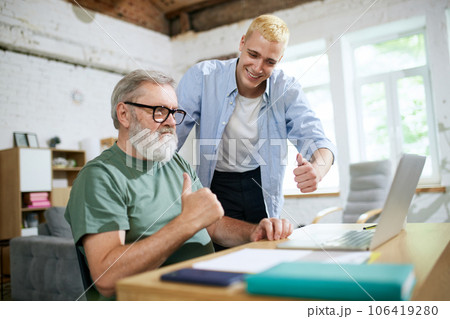 Cooperation of adults and youngsters. Young man helping senior businessman with technological issues on laptop 106419280