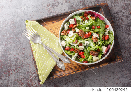 Delicious fresh salad with leaf lettuce, dried cherries, gorgonzola cheese, pecans dressed with vinaigrette sauce close-up in a bowl. Horizontal top view 106420242