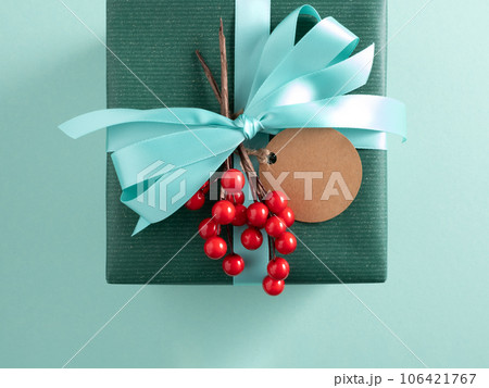 Part of green gift box with turquoise ribbon, craft gift tag and red berries. Turquoise background. 106421767