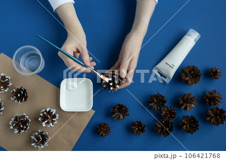 Person painting pine cones Christmas on a blue background. Person painting pine cones Christmas on a blue background. 106421768
