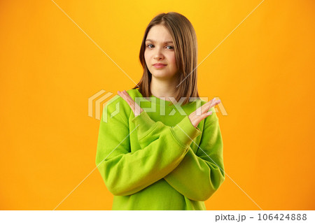 Teen girl shows cross hands gesture, rejecting something over yellow background in studio 106424888